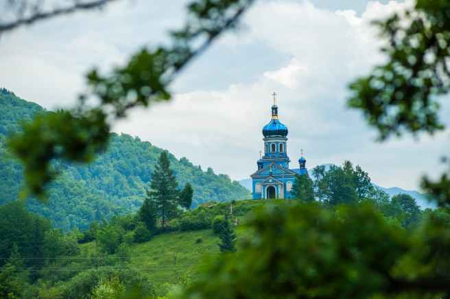 blue dome building surrounded by tall trees taken under white clouds